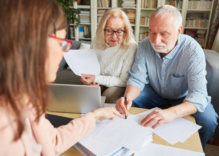 A man and woman sit at a table with a laptop and papers, discussing financial power of attorney documents.